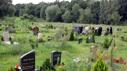 Muslimischer Friedhof mit Grabsteinen, im hintergrund Muslime an einem Grab
