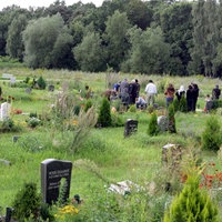 Muslimischer Friedhof mit Grabsteinen, im hintergrund Muslime an einem Grab