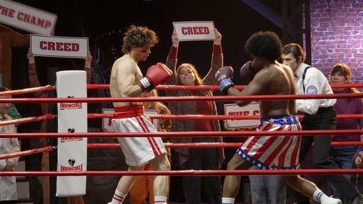 Rocky und sein Gegner Creed stehen im Boxring und werden von Fans angefeuert.