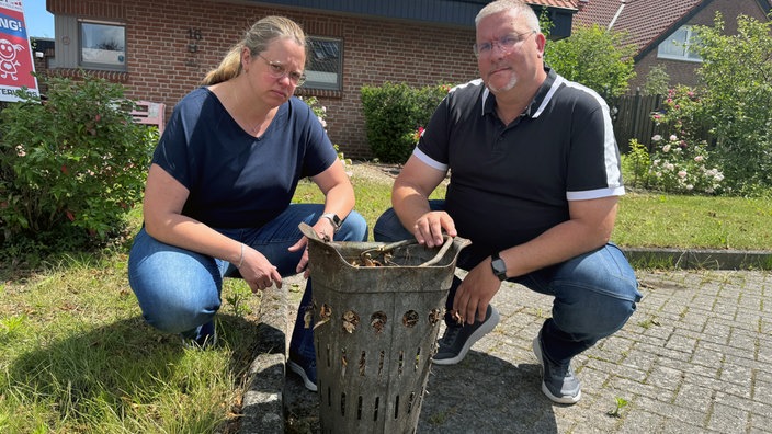 Ina und Andreas Voß hocken hinter einem vollem Fangkorb von einem Gully.