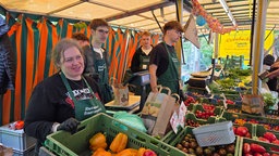 Gemüsestand auf einem Bauernmarkt. Verkäufer stehen hinter dem Stand. 