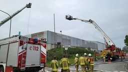 Mehrere Einsatzkräfte der Feuerwehr stehen in Ausrüstung vor einer Lagerhalle