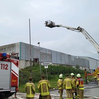 Mehrere Einsatzkräfte der Feuerwehr stehen in Ausrüstung vor einer Lagerhalle
