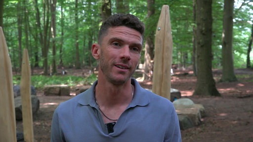 Robin Gosens hat kurze braune Haare und trägt ein graues Oberteil. Hinter ihm stehen Holzpfähle.