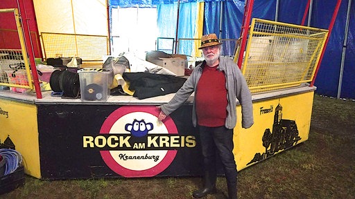 Theo Hünnekes, Vorsitzender des Vereins Rock am Kreis, steht im Zelt vor dem Logo des Festivals