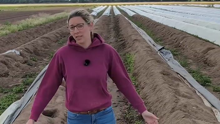 Landwirtin Carola Heyes steht mit einem roten Pulli auf ihrem Spargelfeld und schaut in die Kamera
