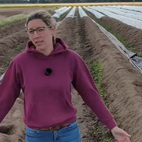 Landwirtin Carola Heyes steht mit einem roten Pulli auf ihrem Spargelfeld und schaut in die Kamera