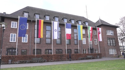 Das Rathaus in Dinslaken hat viele Fenster, ein schwrazes Dach und dunkle Klinkerwände. Davor hängen viele Länderflaggen.