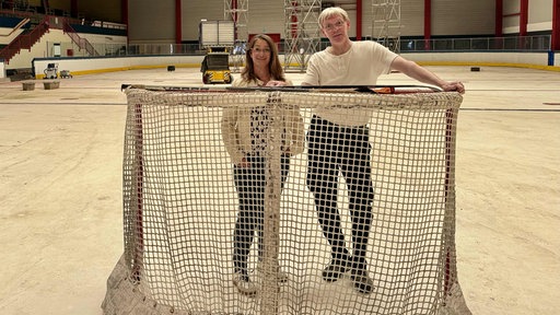 Frau und Mann stehen auf Eisbahn hinter einem Hockey-Tor