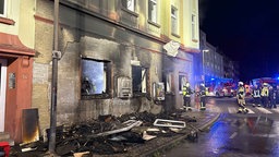 Die Feuerwehr im Einsatz, verkohlter Sperrmüll liegt vor einem verrusten und beschädigten Gebäude