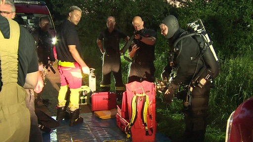 Mehrere Einsatzkräfte der Feuerwehr stehen nebeneinander, ganz rechts ein Taucher in Ganzkörperausrüstung.