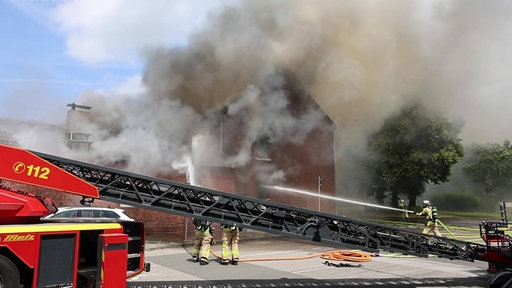 Ein Wohnaus steht im Vollbrand und Feuerwehrleute löschen den Brand