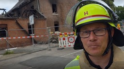 Feuerwehrmann steht vor einem Haus. Das Haus ist abgebrannt.