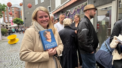 Eine Frau steht mit dem Buch "Freiheit" von Angela Merkel vor einer Buchhandlung, hitner ihr eine lange Schlange