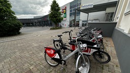Fahrradverleihstation mit mehreren silber-schwarzen Mieträdern der Marke "nextbike" mit dem roten Logo "HeiBi" vor einem modernen Gebäude mit Glassfassade.