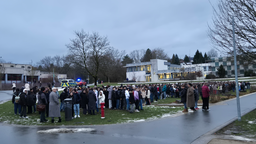Eine große Menschenmenge auf einer Wiese vor einem Schulgebäude. Einsatzfahrzeuge sind im Hintergrund.