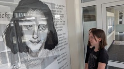 Zwei Schülerinnen betrachten eine Informationstafel zum Leben von Anne Frank.