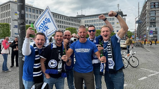 Eine Gruppe Männer jubelt und reißt die Arme hoch.