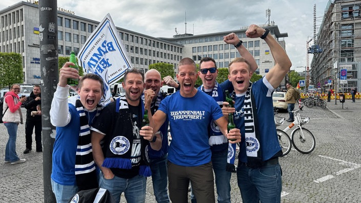 Eine Gruppe Männer jubelt und reißt die Arme hoch.