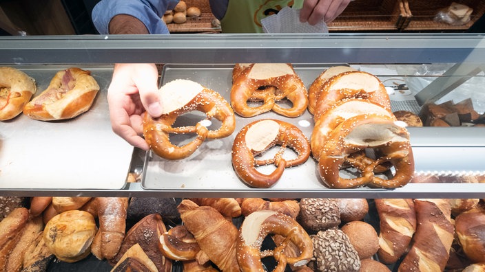 Eine Verkaufstheke in einer Bäckerei ist von oben zu sehen. Eine Hand greift eine Brezel 