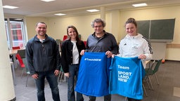Vertreter der Schule und Elternschaft C. Nowack, Jessica Tewes, Clemens Binder, und Johanna Hartmann halten die Trikots hoch.