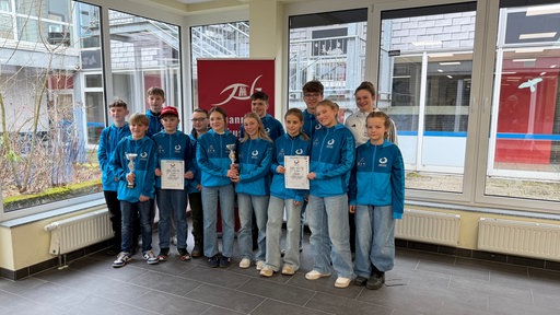 Die Jugendlichen stehen in ihren Trikots beisammen und halten stolz Urkunden und Pokale.