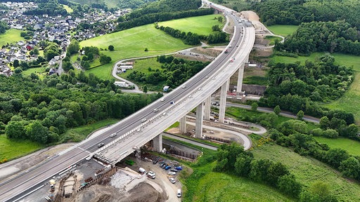 Aus der Luft ist der Neubau einer achtspurigen Autobahnbrücke über ein begrüntes Tal zu sehen.
