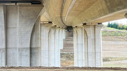 Breite Betonstützen tragen den Oberbau einer Autobahnbrücke, darunter Schutt und Geröll.