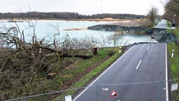 In der Straße klafft ein riesiges Loch, daneben wurden Bäume gefällt, im Hintergrund ist der Sandabbau zu sehen.