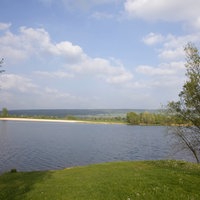 Eine grüne Wiese, dahinter ein blauer See.