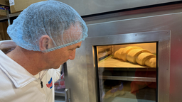 Ein Mann mit Schutzhaube der auf einen Ofen schaut. In dem Ofen wird ein Croissant gebacken.