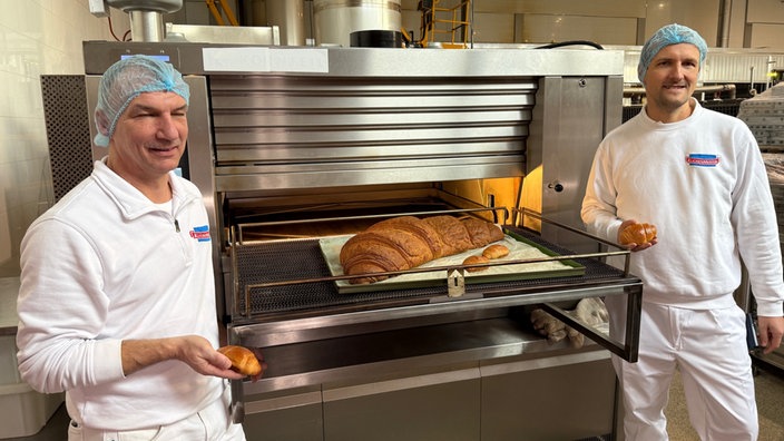 Zwei Bäckermeister stehen vermeintlich neben dem größten Croissants der Welt
