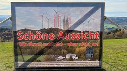 Ein Plakat gegen ein Windrad vor einer weiten Landschaft