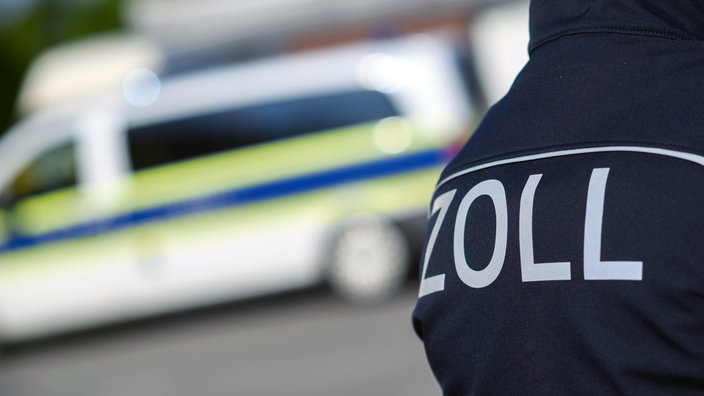 Ein Zollschriftzug auf Uniform vor einem Einsatzwagen.