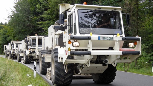 Mehrere Vibro-Trucks, die hintereinander auf einer Landstraße fahren.