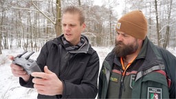 zwei Männer stehen im verschneiten Wald und halten ein Gerät