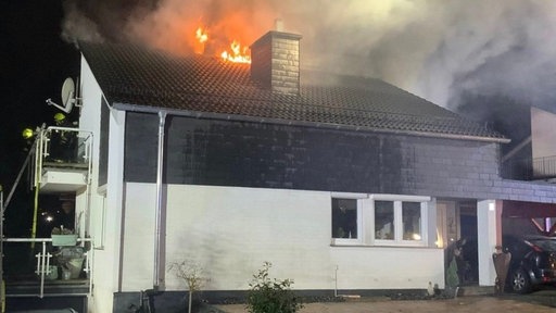 Feuer steigt aus dem Dach eines Zweifamilienhauses heraus, ansonsten ist nur die teilverschieferte Hauswand zu sehen