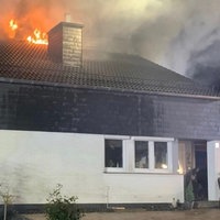 Feuer steigt aus dem Dach eines Zweifamilienhauses heraus, ansonsten ist nur die teilverschieferte Hauswand zu sehen