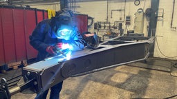 Ein Mitarbeitender führt Schweißarbeiten an einem Metallteil durch
