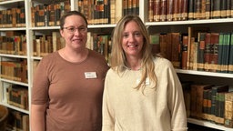Portaitbild von zwei frauen vor Bücherregal