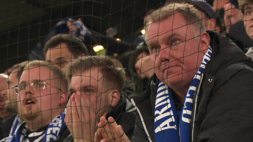 Drei Männer mit Arminia Bielefeld-Schal sitzen am Spielfeldrand und betrachten das Spiel