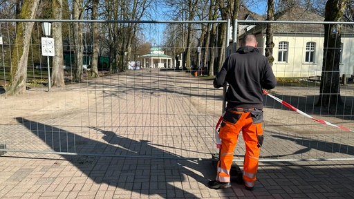 Ein Mann steht vor einem Bauzaun, der einen Bereich absperrt 