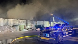 Die Feuerwehr löscht mit einer Drehleiter die qualmende Halle