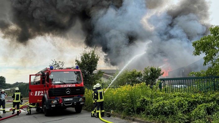 Zwei Feuerwehrleute stehen neben einem Feuerwehrwagen und löschen den Brand.