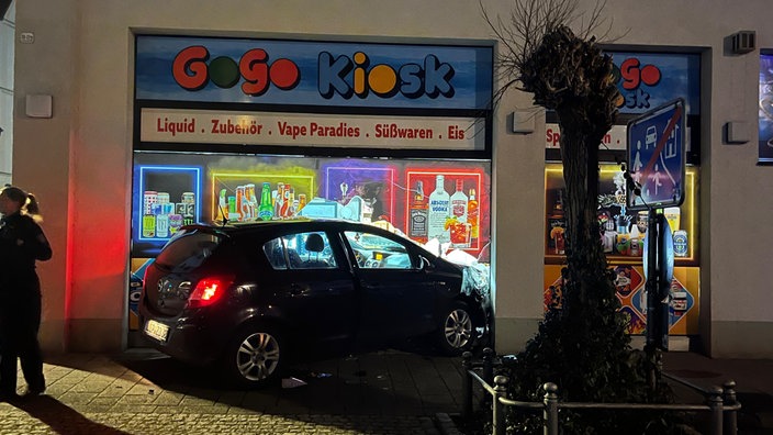 Das Auto, wie es mit der vorderen Hälfte im zerstörten Schaufenster des Kiosk steht.