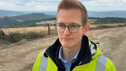 Ein Mann mit gelber Warnjacke steht auf einem Feld 