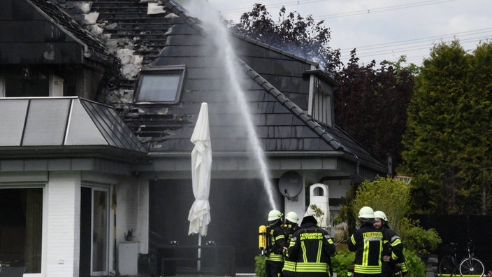 Feuerwehrleute richten einen Wasserstrahl auf ein teilweise zerstörtes Dach eines Wohnhauses.