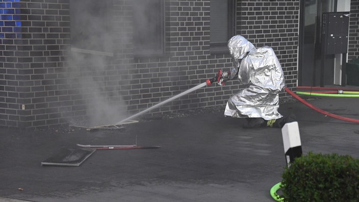 Ein Feuerwehrmann in Schutzkleidung richtet den Wasserschlauch von außerhalb des Gebäudes in den Keller, um den Brand zu löschen
