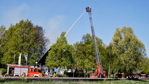 Feuerwehrautos mit Leiterwagen vor einem von Bäumen umgebenen Haus