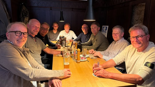 Ein Gruppe von Männern sitzt an einem Tisch und trinkt Bier.